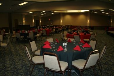 A round table with a black table cloth and red napkins on it and chairs all around the table